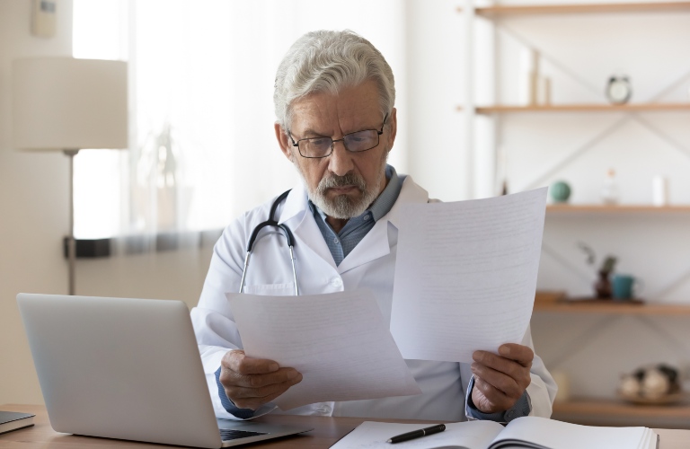 Doctor reviewing paperwork in front of a laptop